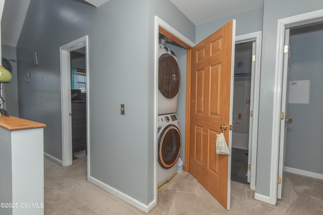 laundry room with stacked washing machine and dryer, light colored carpet, and baseboards