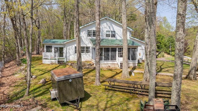 rear view of property with a sunroom, a lawn, metal roof, and a view of trees