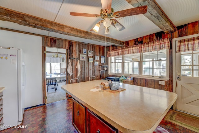 kitchen featuring freestanding refrigerator, wood walls, beam ceiling, healthy amount of natural light, and a ceiling fan