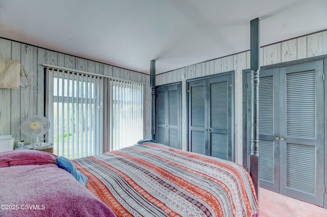 carpeted bedroom featuring multiple closets and wood walls
