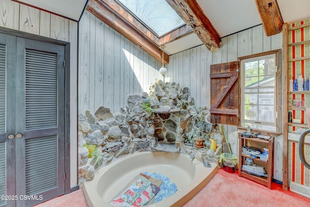 bathroom featuring wood walls, a skylight, and beamed ceiling