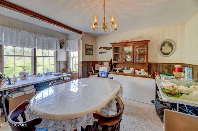 dining space with wallpapered walls, a wainscoted wall, a chandelier, and beam ceiling