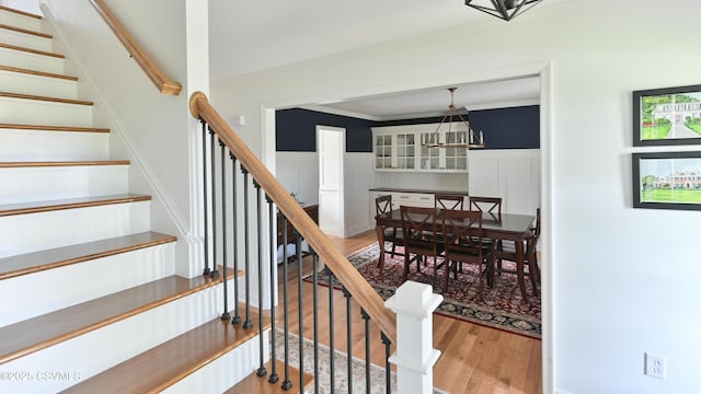 stairs featuring wood finished floors, wainscoting, ornamental molding, and a decorative wall