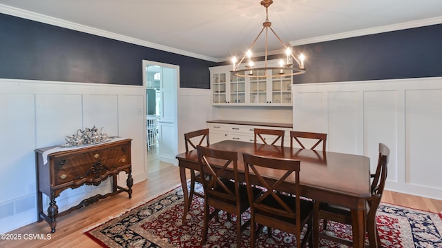 dining area with a decorative wall, a chandelier, light wood-type flooring, crown molding, and wainscoting