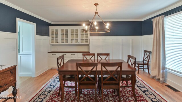 dining space featuring a chandelier, a decorative wall, light wood-style floors, a wainscoted wall, and crown molding