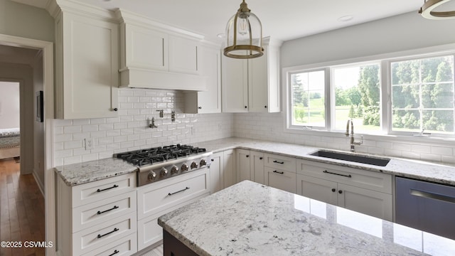 kitchen featuring stainless steel appliances, a sink, white cabinetry, wood finished floors, and light stone countertops