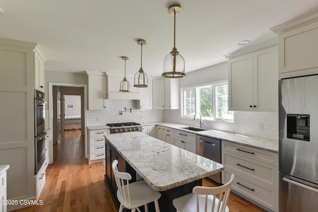 kitchen featuring appliances with stainless steel finishes, a sink, a center island, backsplash, and a kitchen breakfast bar