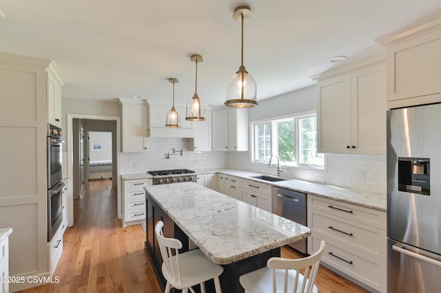 kitchen with stainless steel appliances, a sink, a kitchen island, decorative backsplash, and light wood-style floors