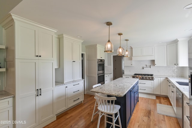 kitchen with stainless steel appliances, a kitchen island, decorative backsplash, light wood-type flooring, and white cabinetry