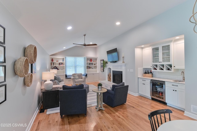living room with wine cooler, wet bar, light wood finished floors, a fireplace with raised hearth, and vaulted ceiling