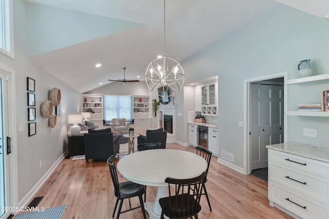 dining area featuring lofted ceiling, wine cooler, light wood-style flooring, a glass covered fireplace, and a chandelier