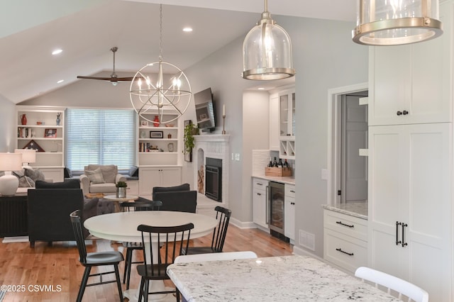 dining room featuring beverage cooler, vaulted ceiling, light wood-type flooring, a chandelier, and a fireplace
