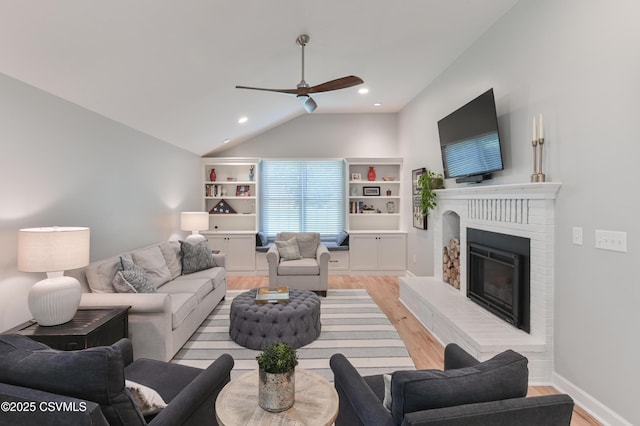 living area featuring light wood-style flooring, a ceiling fan, vaulted ceiling, a fireplace, and recessed lighting