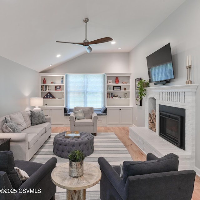 living area featuring lofted ceiling, light wood-style flooring, a brick fireplace, ceiling fan, and recessed lighting