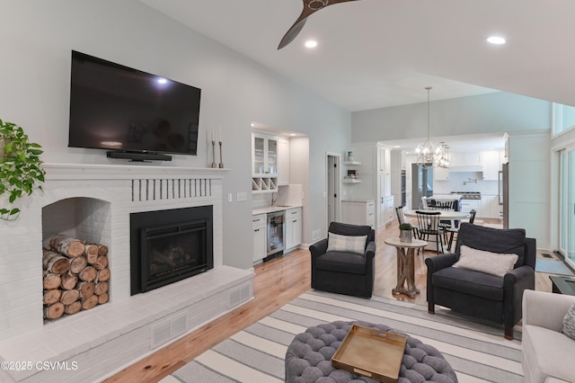 living area with beverage cooler, a fireplace, light wood-style floors, ceiling fan, and a chandelier