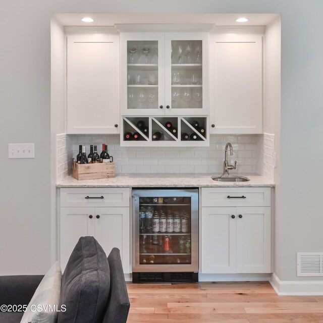 indoor wet bar featuring wine cooler, tasteful backsplash, light wood-style floors, recessed lighting, and baseboards