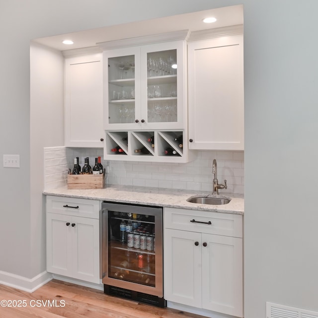 indoor wet bar featuring beverage cooler, tasteful backsplash, light wood finished floors, recessed lighting, and baseboards