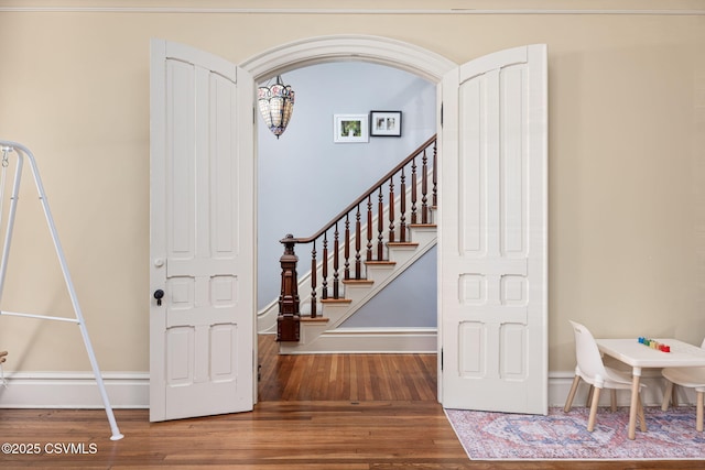 stairs featuring wood finished floors, arched walkways, and baseboards