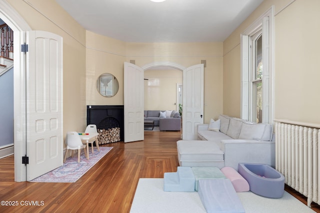 living area with radiator, arched walkways, a fireplace, wood finished floors, and stairway