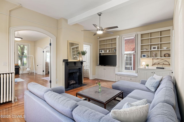 living room with ceiling fan, radiator heating unit, arched walkways, a fireplace with flush hearth, and wood finished floors