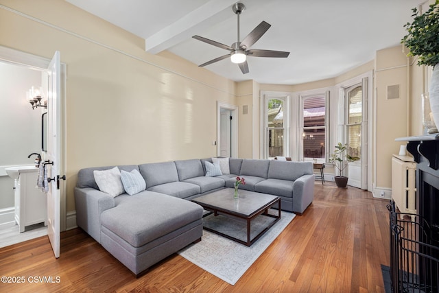 living room featuring a ceiling fan, light wood-style floors, beam ceiling, and baseboards