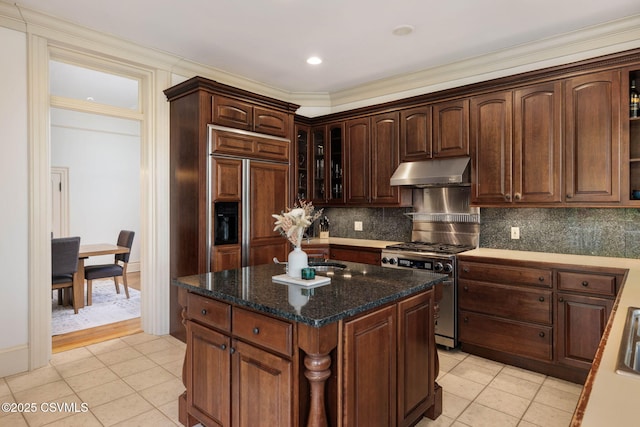 kitchen with under cabinet range hood, gas stove, paneled built in fridge, decorative backsplash, and ornamental molding