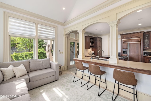 kitchen featuring decorative columns, paneled built in refrigerator, a sink, arched walkways, and a breakfast bar area