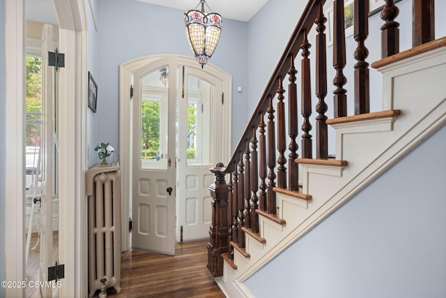 foyer featuring radiator, arched walkways, wood finished floors, stairway, and a chandelier