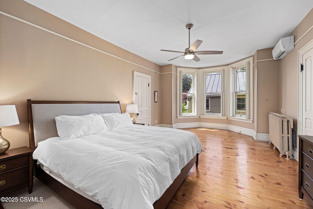 bedroom with radiator heating unit, a wall unit AC, hardwood / wood-style flooring, baseboards, and ceiling fan