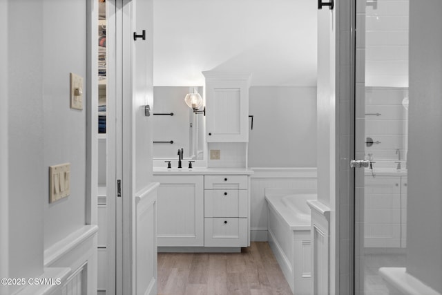 full bath with wood finished floors, a stall shower, a garden tub, vanity, and a wainscoted wall