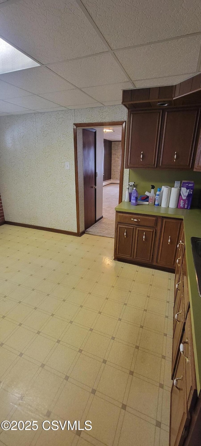 kitchen featuring light flooring, a drop ceiling, baseboards, light countertops, and a sink