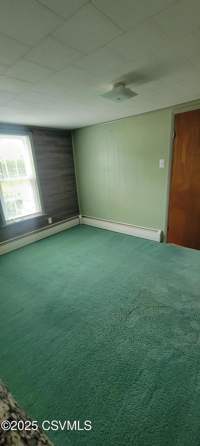 carpeted spare room with baseboard heating and wooden walls