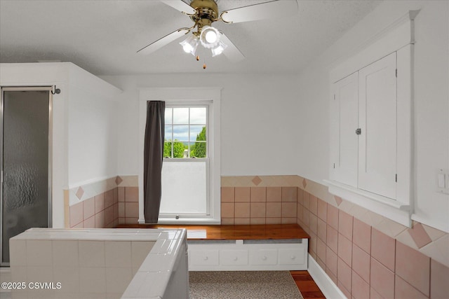 288 Broadway St, Turbotville, PA 17772 - bathroom featuring a stall shower, a ceiling fan, wood finished floors, tile walls, and wainscoting