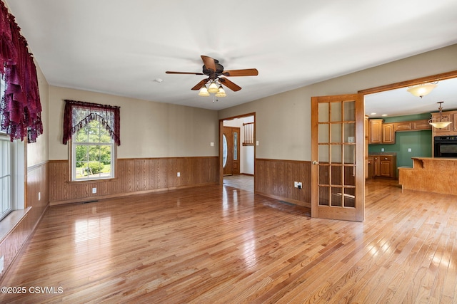 620 Sunset Dr, Bloomsburg, PA 17815 - unfurnished living room featuring wainscoting, light wood-type flooring, wooden walls, french doors, and ceiling fan