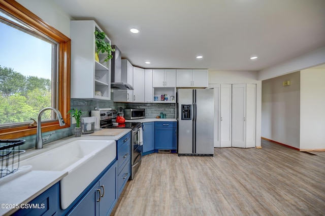 67 Center School Rd, Elysburg, PA 17824 - kitchen featuring appliances with stainless steel finishes, blue cabinetry, wall chimney range hood, open shelves, and light countertops
