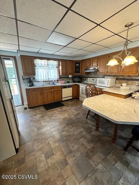1030 Orange St, Berwick, PA 18603 - kitchen with white appliances, under cabinet range hood, light countertops, brown cabinets, and a drop ceiling