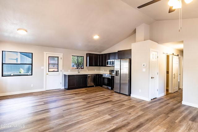 kitchen featuring appliances with stainless steel finishes, a barn door, sink, dark brown cabinetry, and lofted ceiling