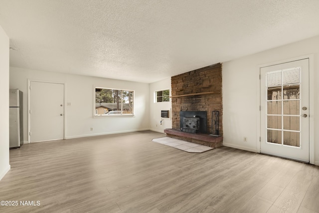 unfurnished living room featuring light hardwood / wood-style floors, a wood stove, and a textured ceiling