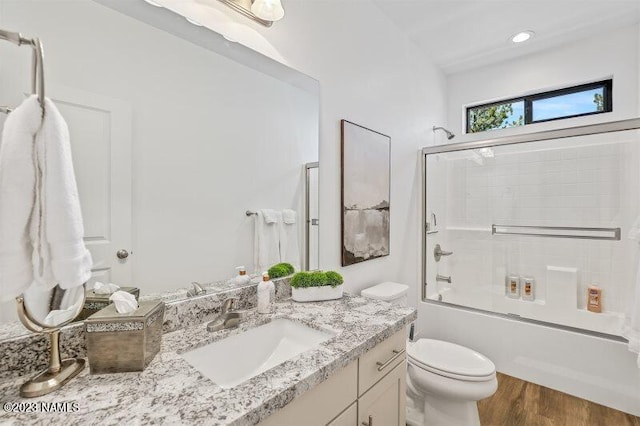 full bathroom with wood-type flooring, bath / shower combo with glass door, toilet, and vanity