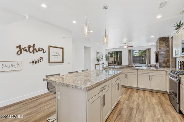 kitchen with light stone countertops, a center island, gas stove, light hardwood / wood-style floors, and a breakfast bar area