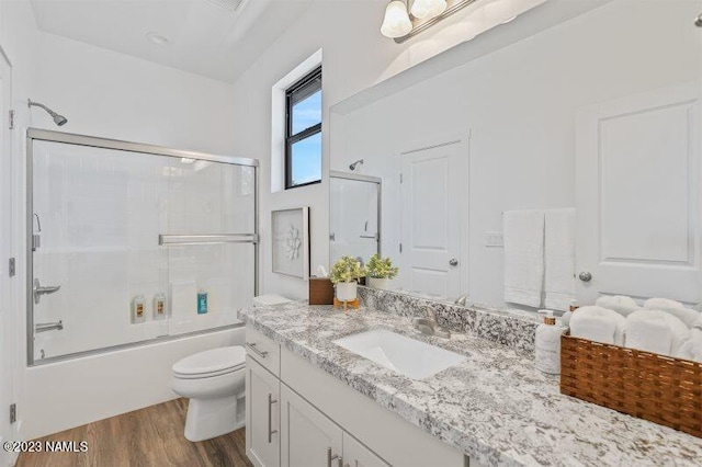 full bathroom with wood-type flooring, combined bath / shower with glass door, vanity, and toilet