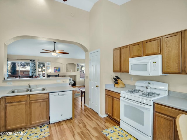 kitchen featuring sink, white appliances, ceiling fan, a towering ceiling, and light wood-type flooring