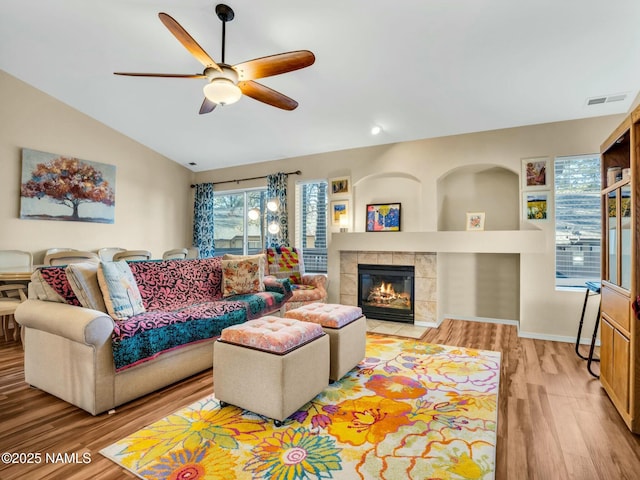 living room featuring a tile fireplace, built in features, lofted ceiling, ceiling fan, and light wood-type flooring