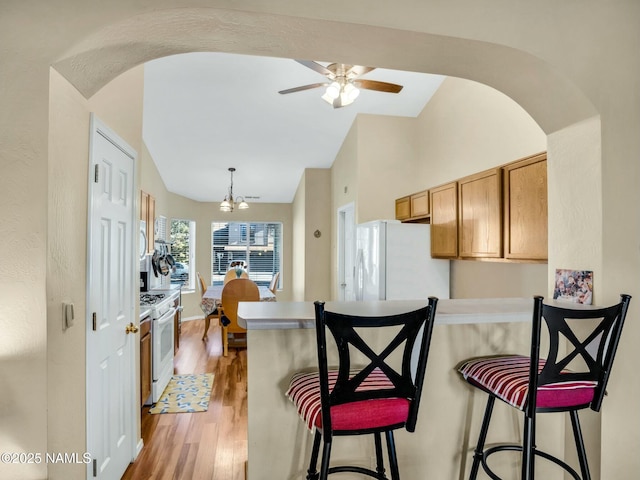 kitchen with white appliances, hardwood / wood-style flooring, hanging light fixtures, a kitchen breakfast bar, and vaulted ceiling