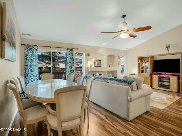 living room with ceiling fan, a fireplace, vaulted ceiling, and light hardwood / wood-style flooring