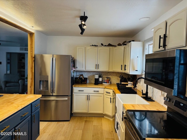 kitchen with butcher block countertops, appliances with stainless steel finishes, decorative backsplash, and blue cabinets