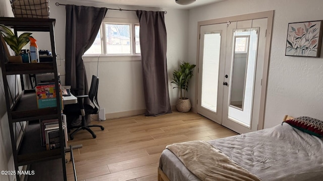 bedroom with french doors, light wood-type flooring, baseboards, a textured wall, and an office area
