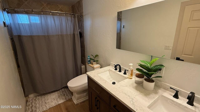 bathroom with wood finished floors, toilet, a textured wall, and double vanity