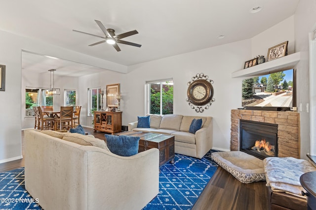 living room featuring a fireplace, dark wood-type flooring, and ceiling fan with notable chandelier