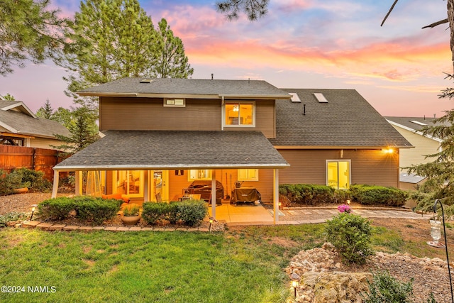 back house at dusk with a patio and a yard